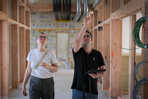 Un ingénieur CVC montrent à une collègue Inddigo les points solutions mise en place pour le Chauffage, la Ventilation et la Climatisation dans l’ école en bois et paille de Feysin.
